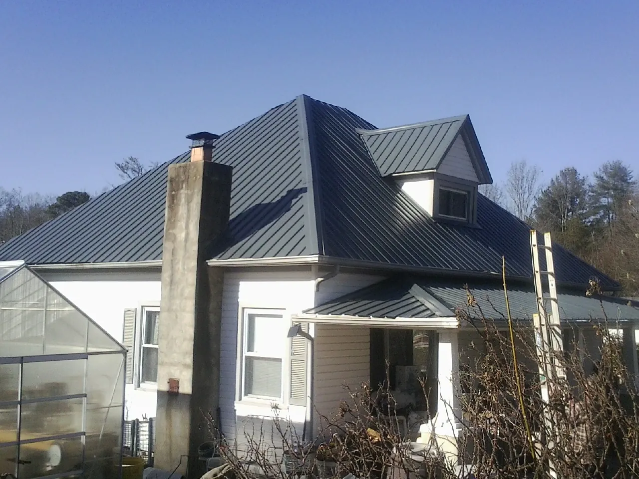 Dark blue standing seam metal roof on a white farmhouse with dormer — Slate & Tile Roof Repair by Roofing Brothers in Belvue