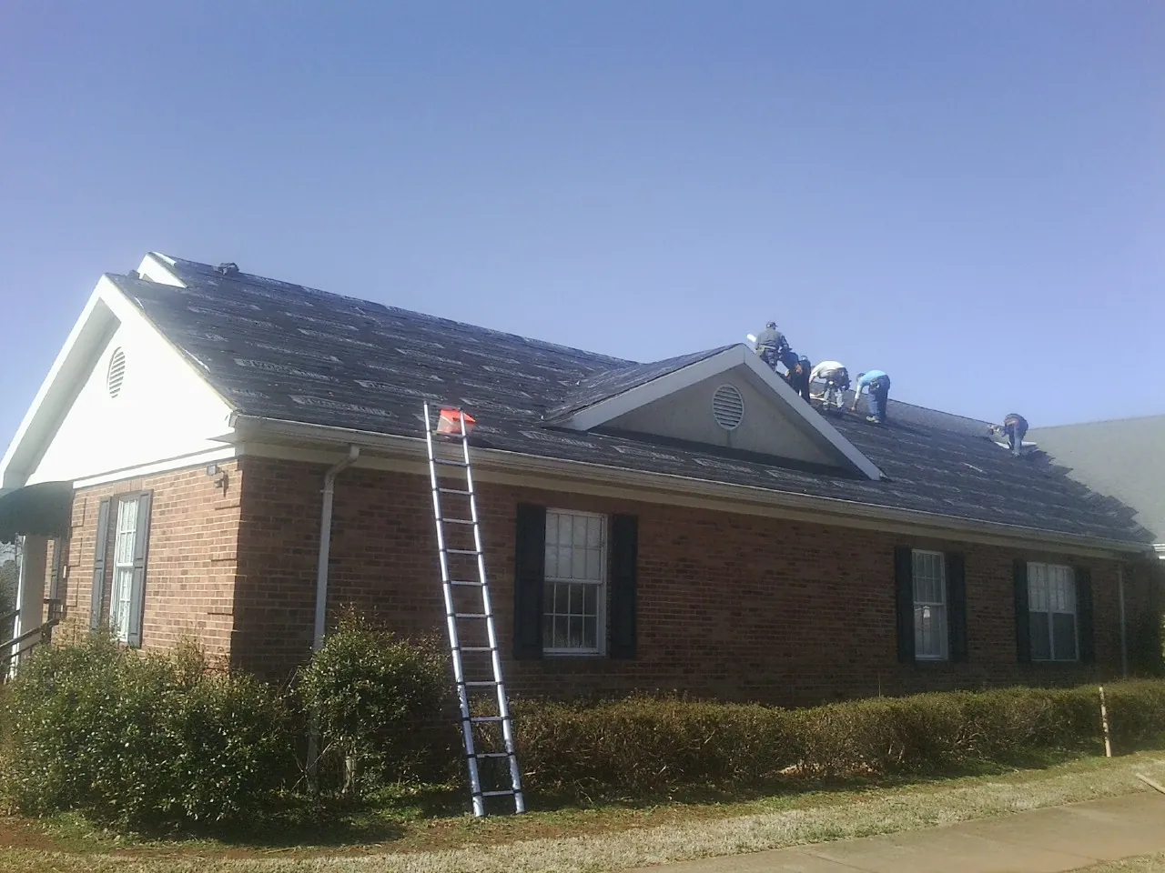 Crew tearing shingles off a brick ranch roof with a ladder set — Emergency Roof Repair work by our crew in Belvue