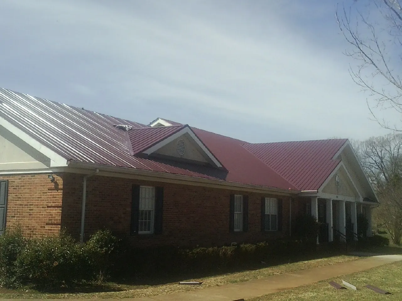 Red metal roof with gabled entries on a long brick building, from a Hail Damage Roof Repair job in Belvue