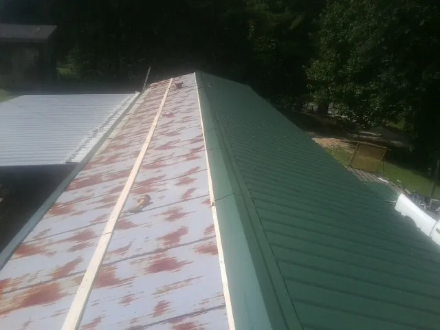 Old rusted panels beside newly installed green metal roofing — Wind Damage Roof Repair by Roofing Brothers in Belvue