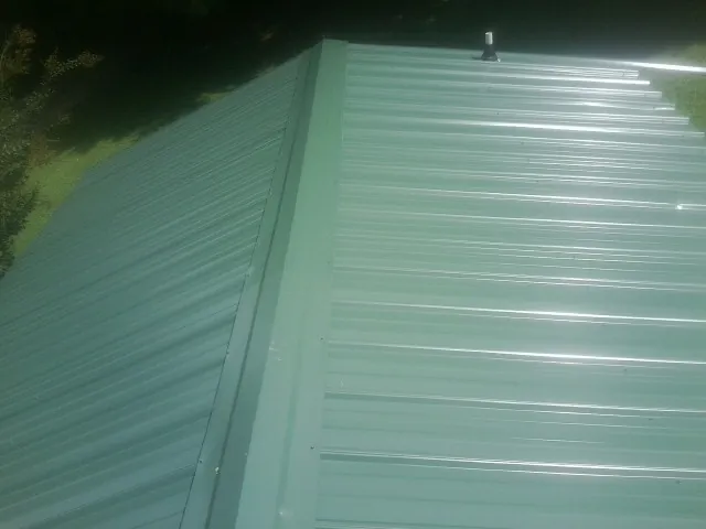 New green metal panels meeting at the ridge of a roof — Flat Roof Repair work by our crew in Belvue