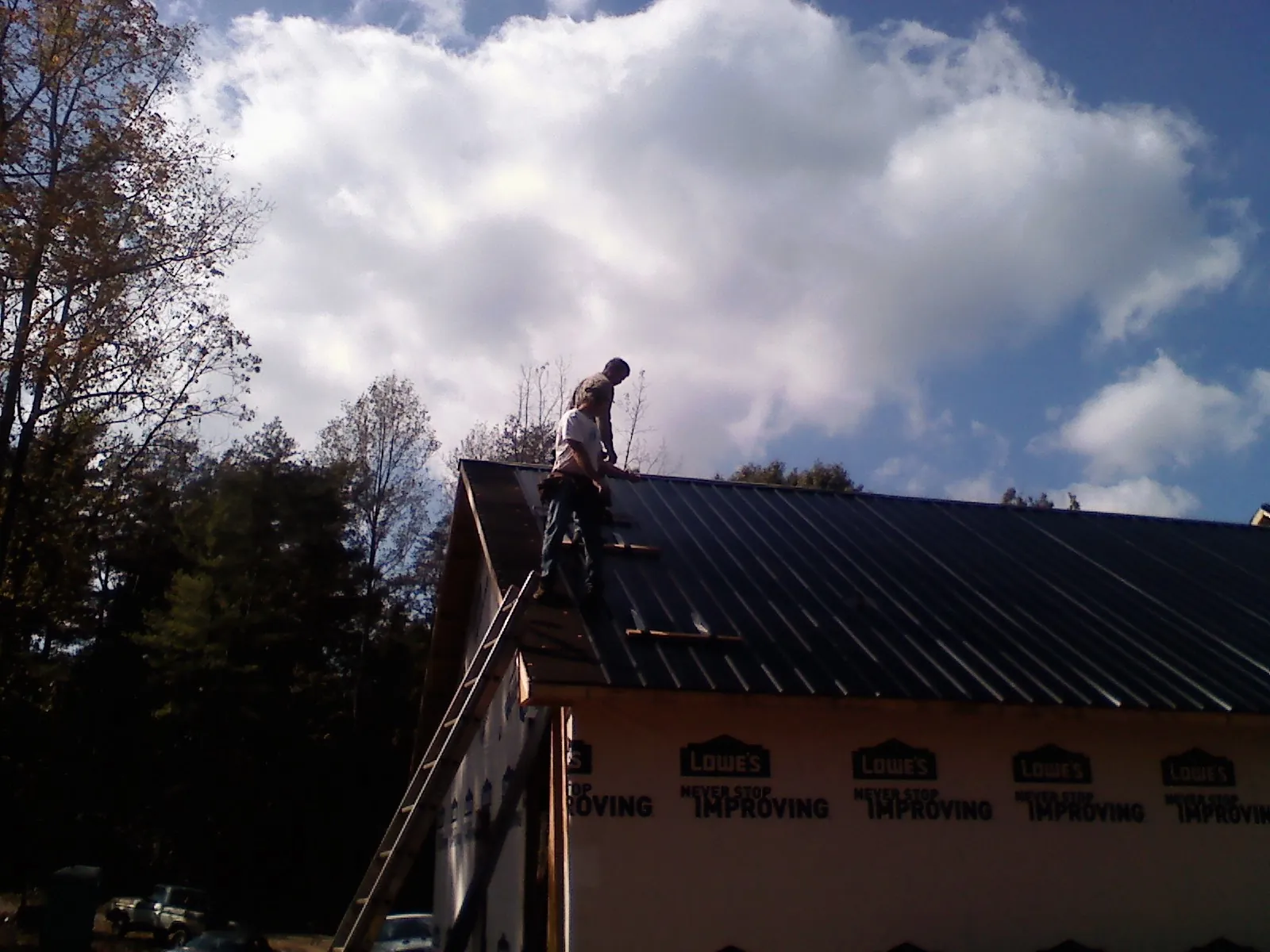 Roofer fastening dark metal panels high against a cloudy sky, from a Roof Inspection job in Belvue