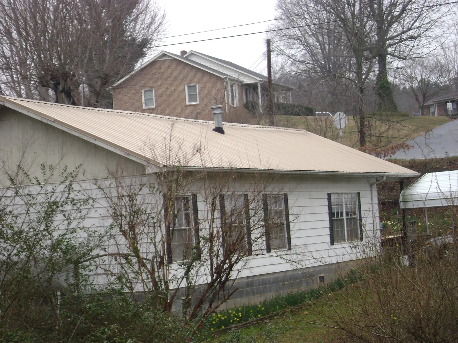 Tan metal roof on a white sided house set into a hillside — Commercial Roofing by Roofing Brothers in Belvue