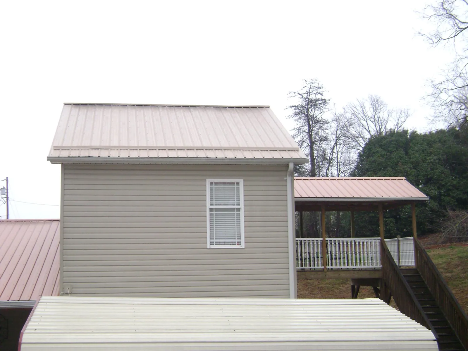 Tan metal roofs on a two story addition and attached porch, from a Roof Replacement job in Belvue